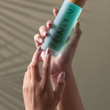 Hand holding KI'OLAL Mist with natural shadow backdrop