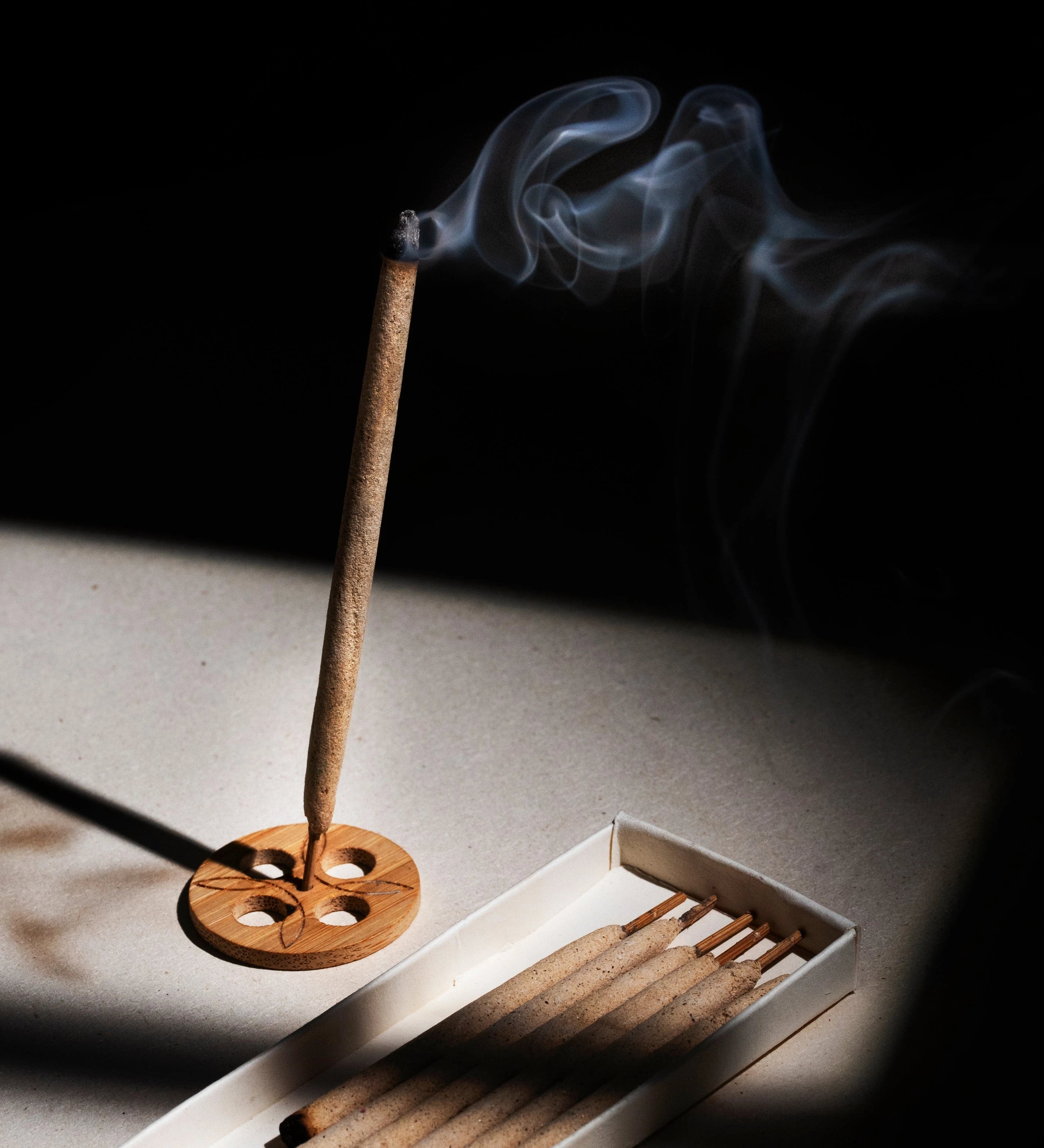 Burning KI'OLAL incense stick with smoke, minimalist tranquility aesthetic